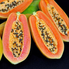 Close-up of papayas, both whole and halved, on a dark background