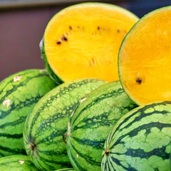 Close-up of green watermelons with a yellow watermelon half on a blurred background