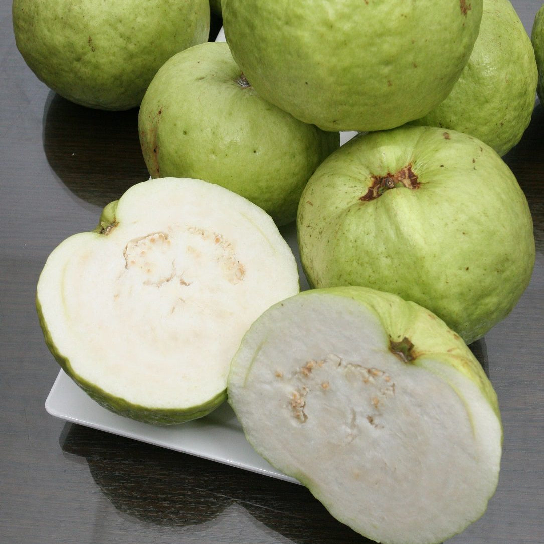 Green guava fruits with one cut open on a reflective surface